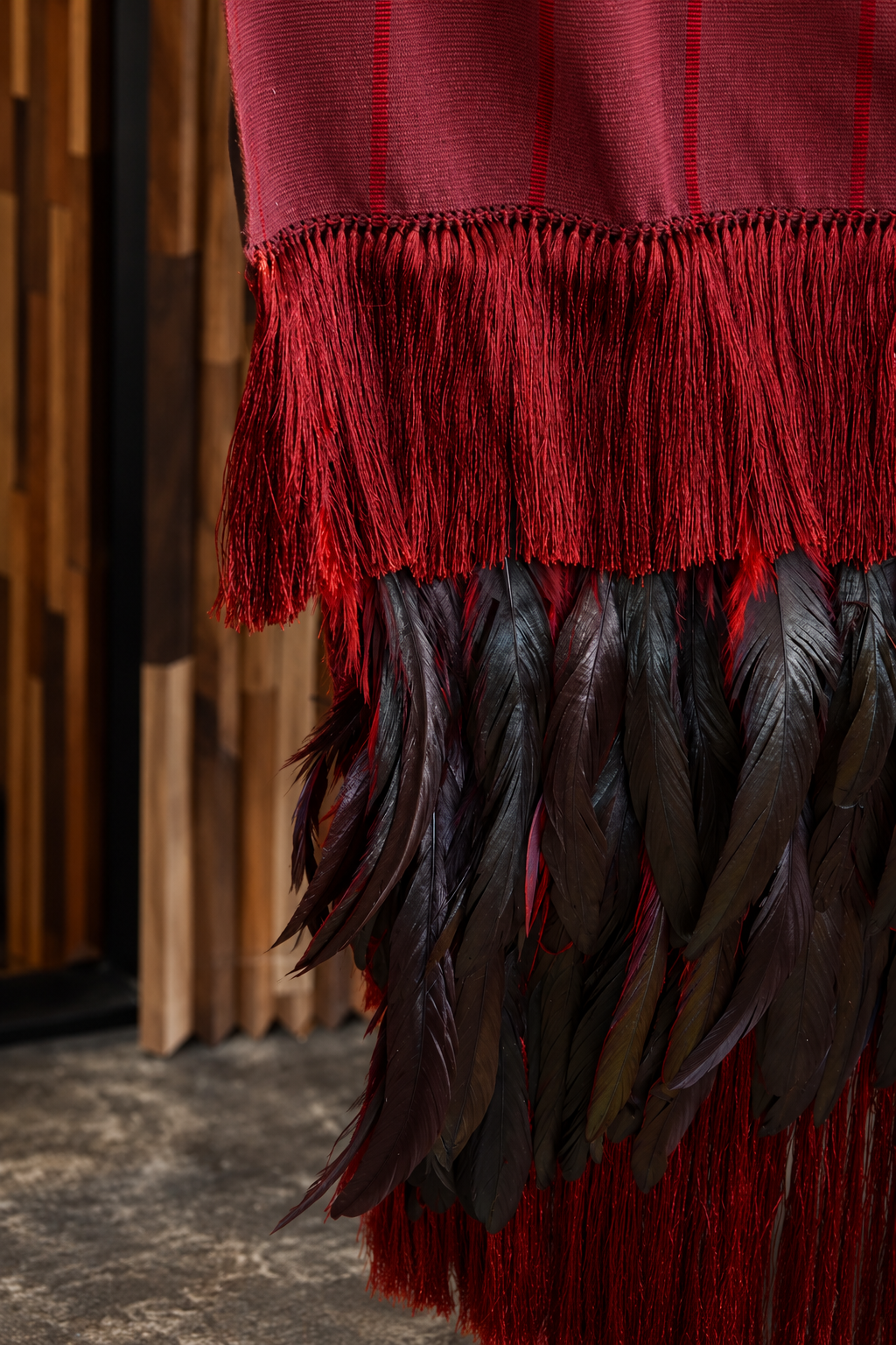 Crimson and black feather rebozo with burgundy fringe, elegant wearables by Embajada Craft showcasing vibrant feathers and detailed craftsmanship.