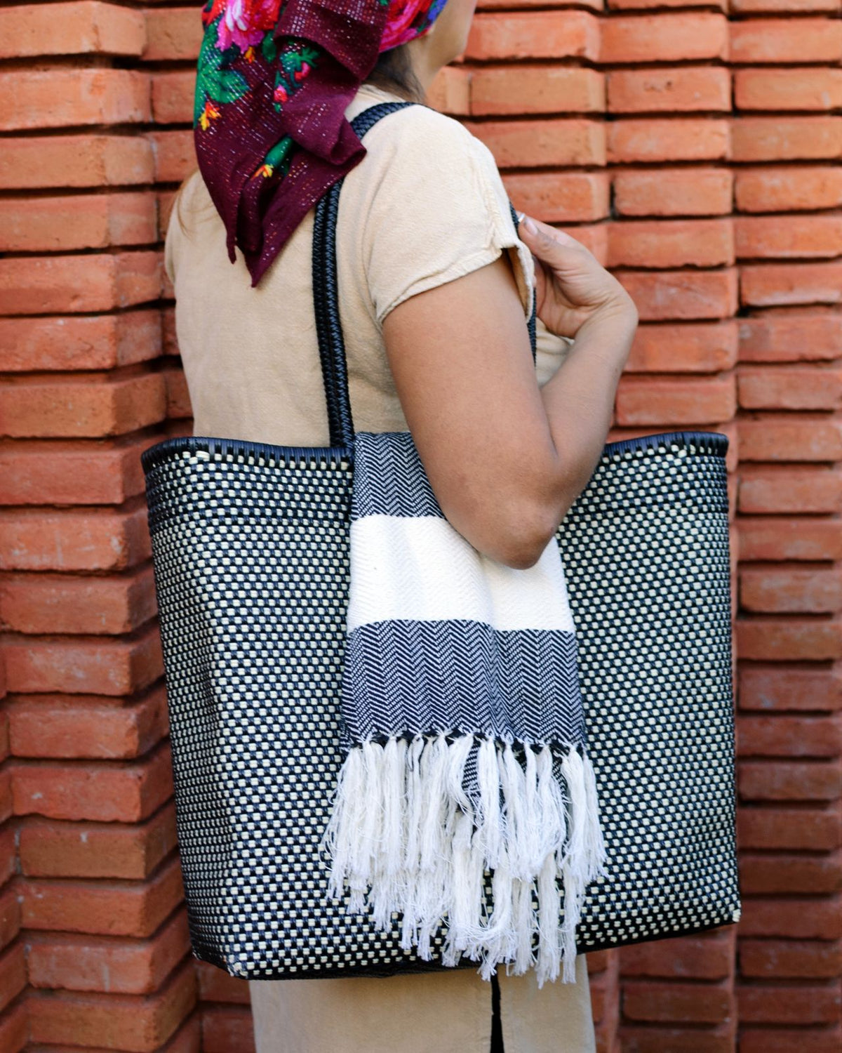 La Embajada Tlacochahuaya Lake Bag featuring woven fabric with colorful patterns and leather accents, displayed in natural light.