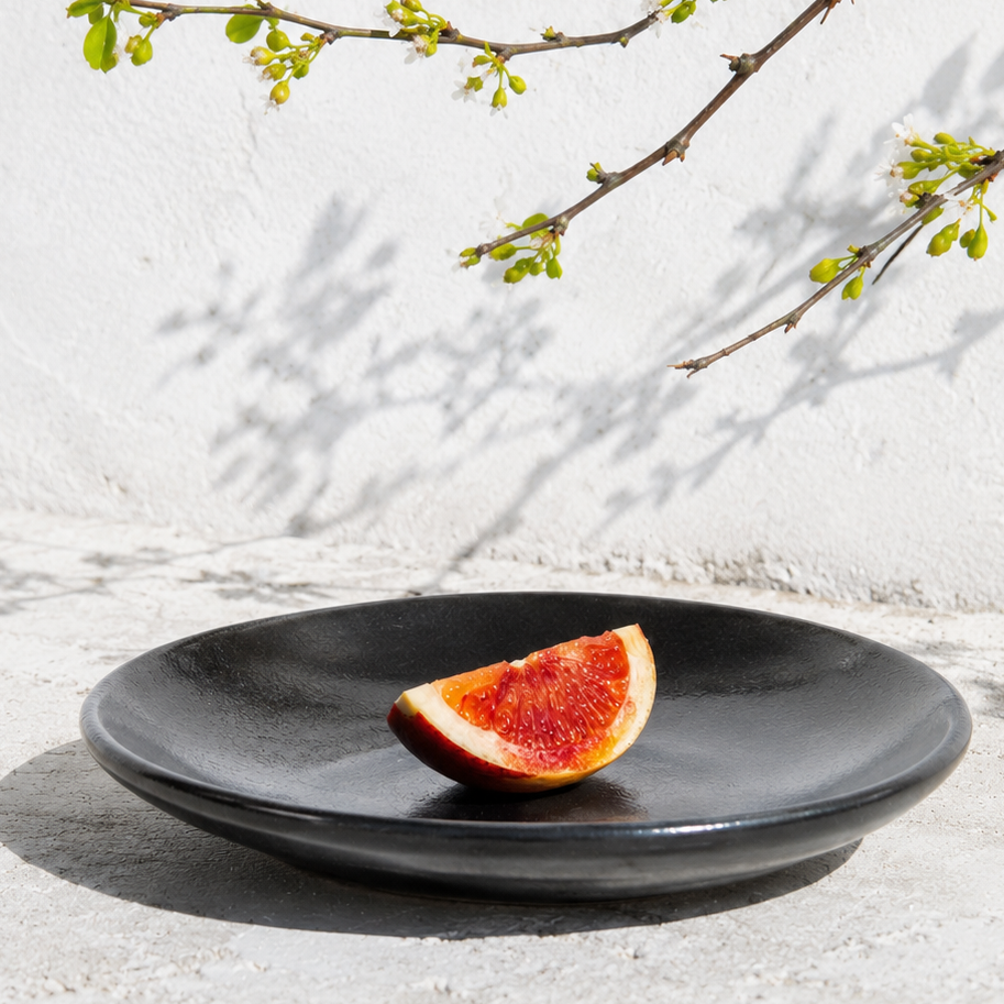 Black plate with a slice of fig on a light surface with a branch in the background