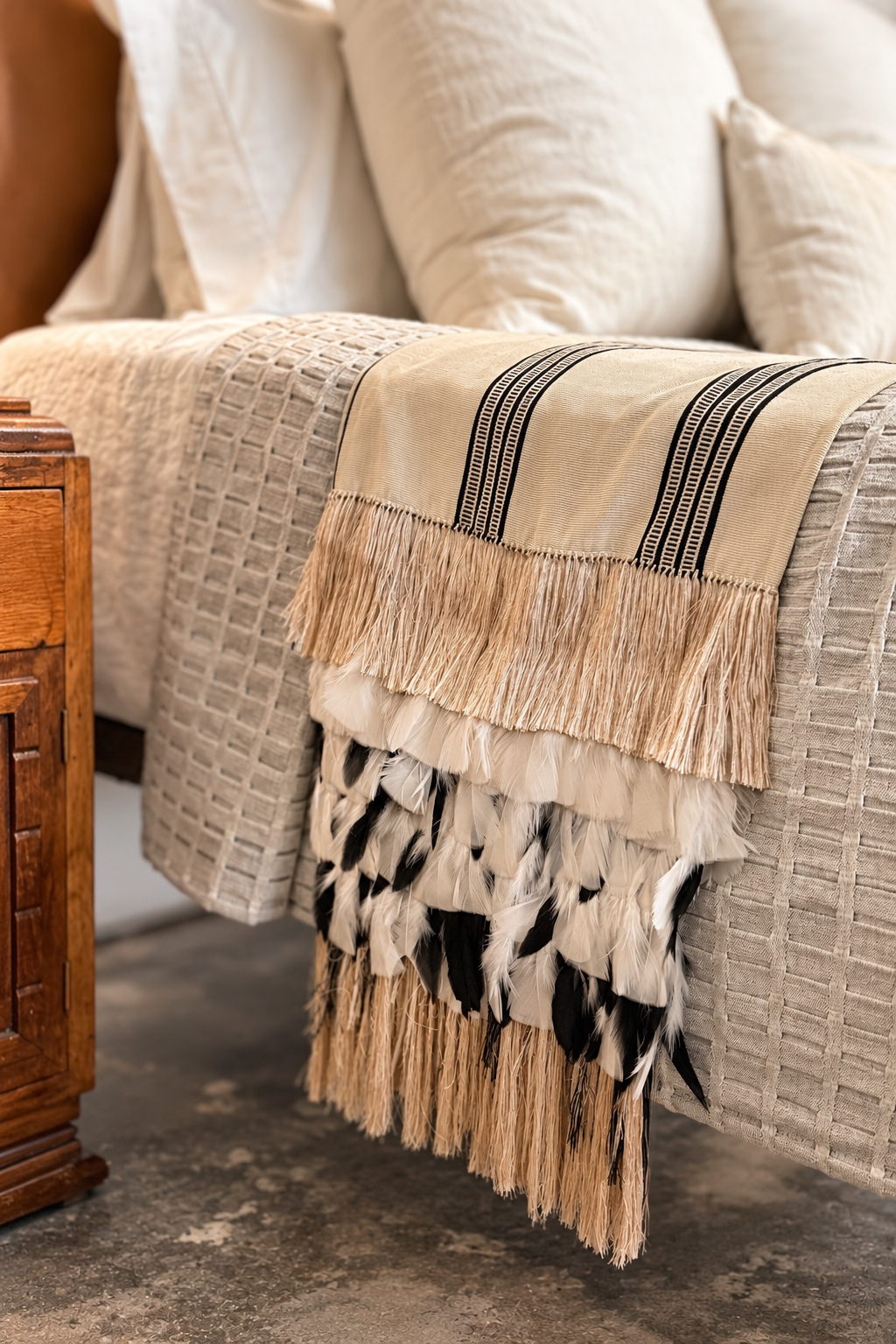 Textured ivory, charcoal, and camel feather rebozo with fringed edges, displayed on a bed for a stylish and cozy look.